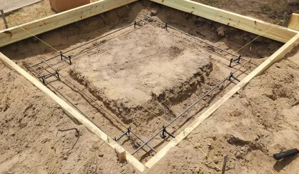 A diamond shaped concrete form with rebar, elevation supports, and string lines set in a dirt foundation.